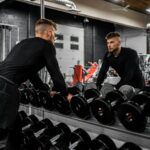 Man looking in mirror while standing over dumbbells in gym, representing strength training and focus