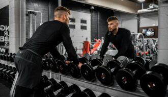 Man looking in mirror while standing over dumbbells in gym, representing strength training and focus