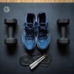 Pair of dumbbells, blue running shoes, and jump rope on a black workout mat for at-home leg workouts
